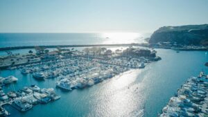 Scenic view of yachts docked at a marina with the ocean horizon and sunlit waters.